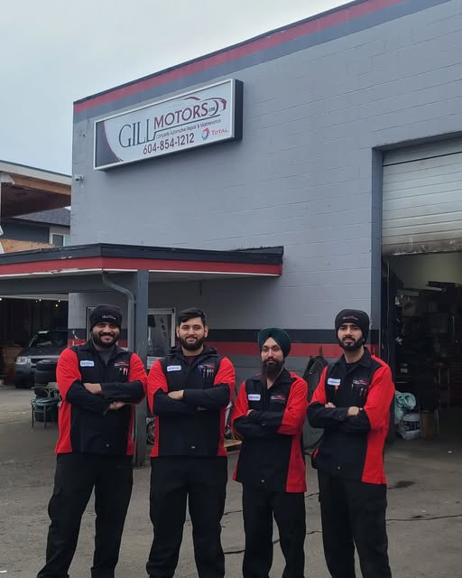 Four people in Gill Motors uniforms outside the shop beneath its sign