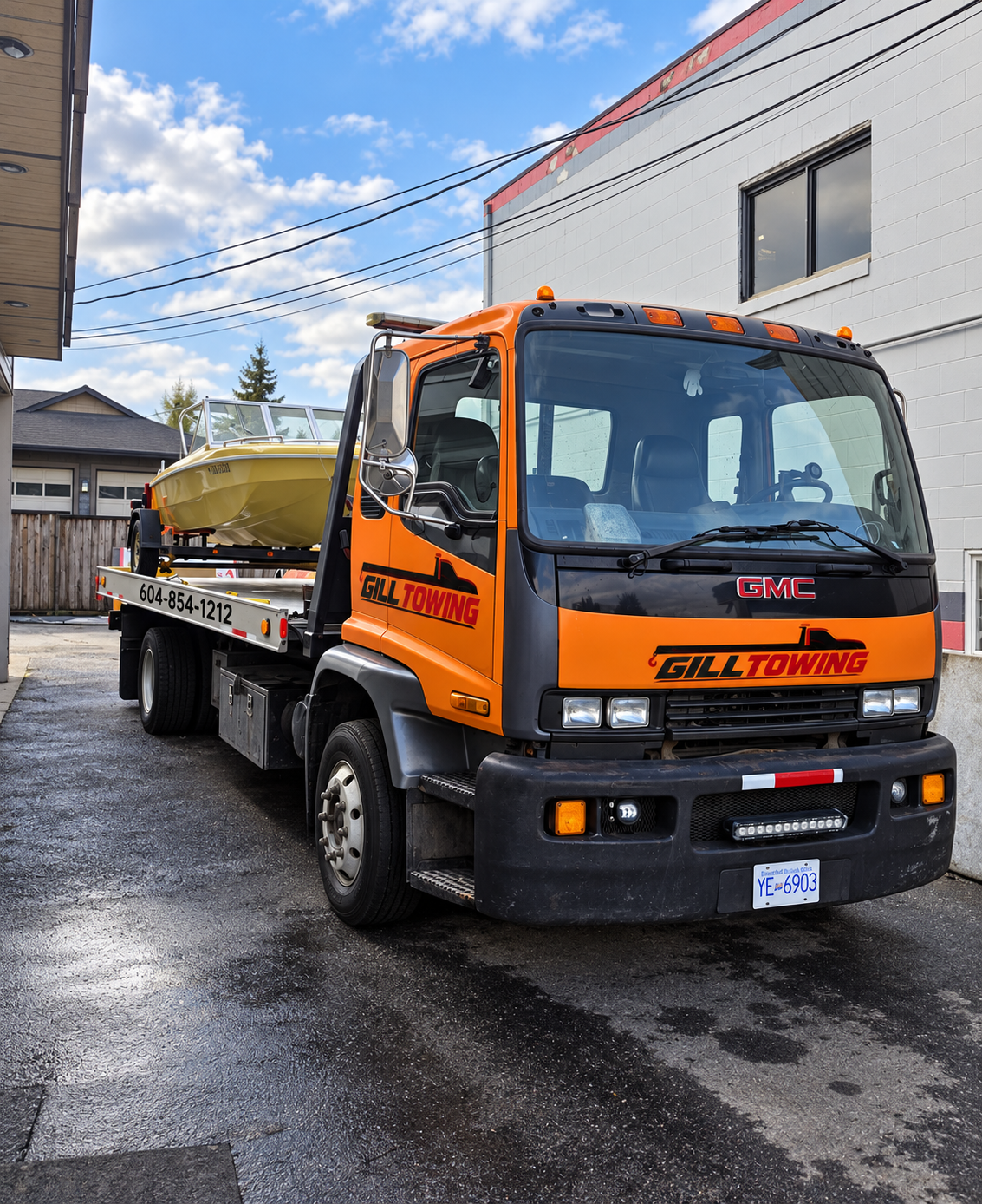 Orange GMC flatbed tow truck with Gill Towing branding, carrying a boat